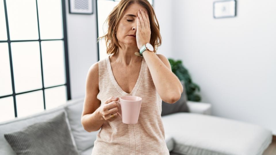 Frau mit Kaffeetasse und Hand auf den geschlossenen Augen scheint chronisch müde zu sein