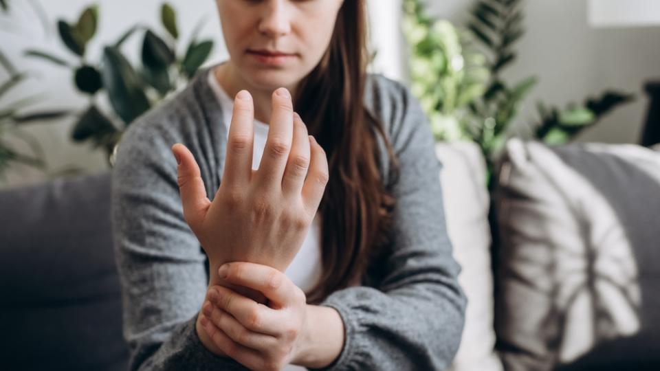 Frau hält sich schmerzverzerrt das Handgelenk und braucht eine Rheuma-Behandlung