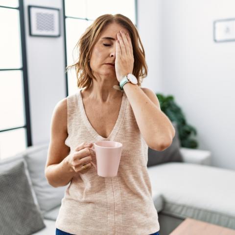 Frau mit Kaffeetasse und Hand auf den geschlossenen Augen scheint chronisch müde zu sein